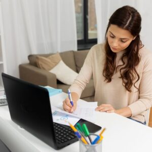 person taking notes in front of laptop